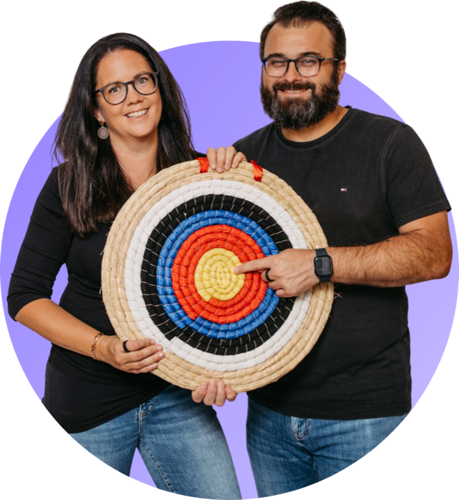 Romana and Florian Hieß holding an archery target, he pointing at the centre